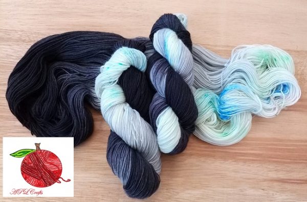 Hugs From Grandma is a swirl of gradient black to grey with speckles of blue, deep green, aqua, and a small bit of pink sitting on a bed of cream.